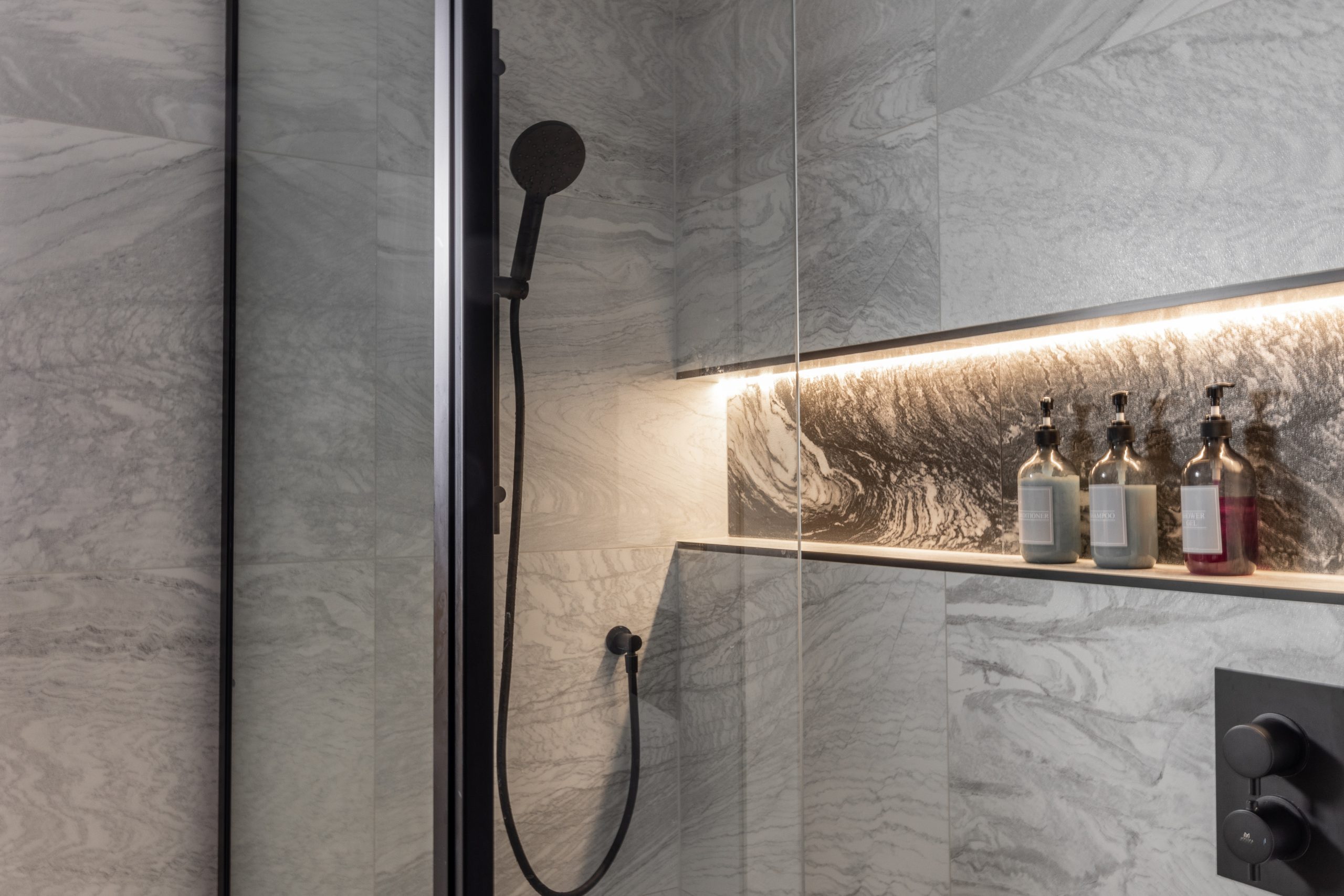 shower cubicle with black shower head and products on a shelf